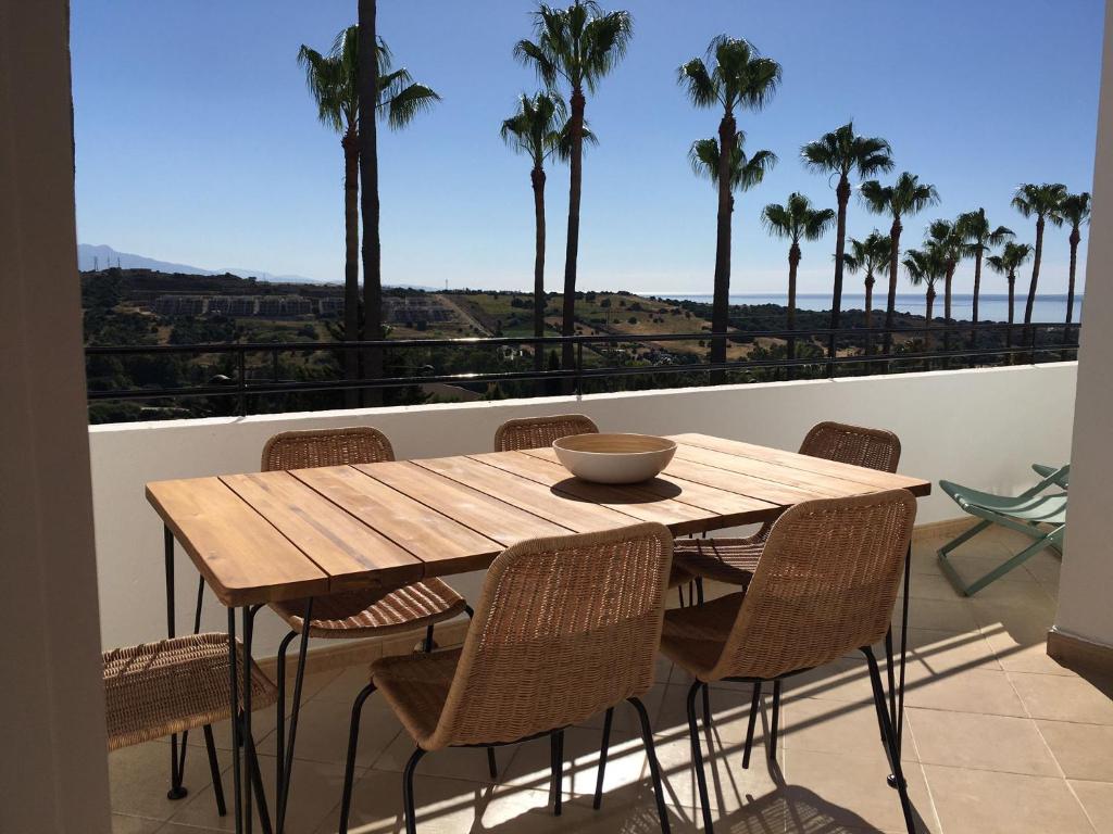 a wooden table and chairs on a balcony with palm trees at Estepona Golf Apartment in Estepona