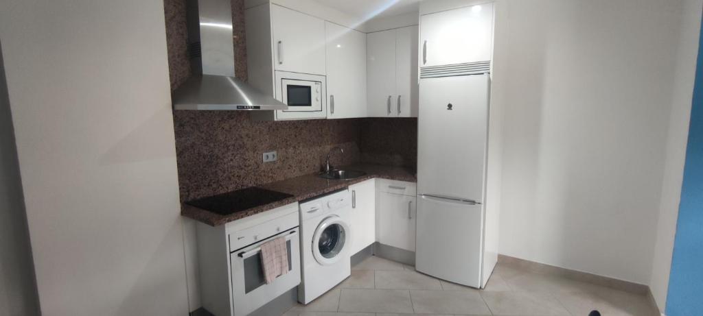 a kitchen with white cabinets and a washer and dryer at Apartamentos Cala Azul La Móra in Tarragona