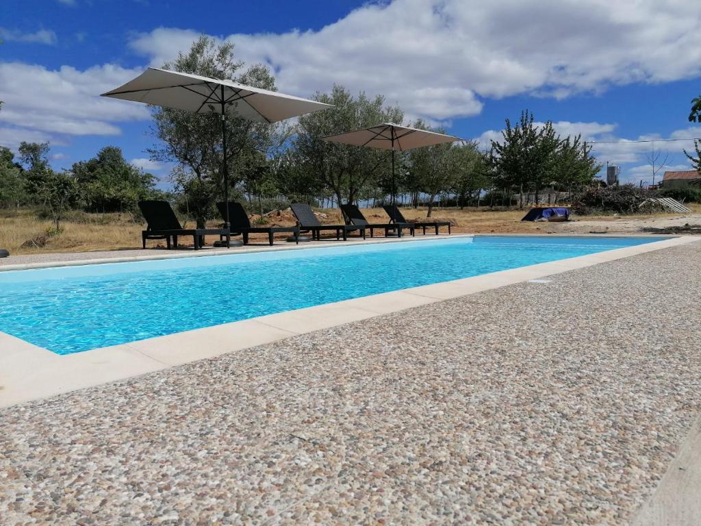 a swimming pool with chairs and umbrellas in a yard at Casa das Indrineiras in Mogadouro