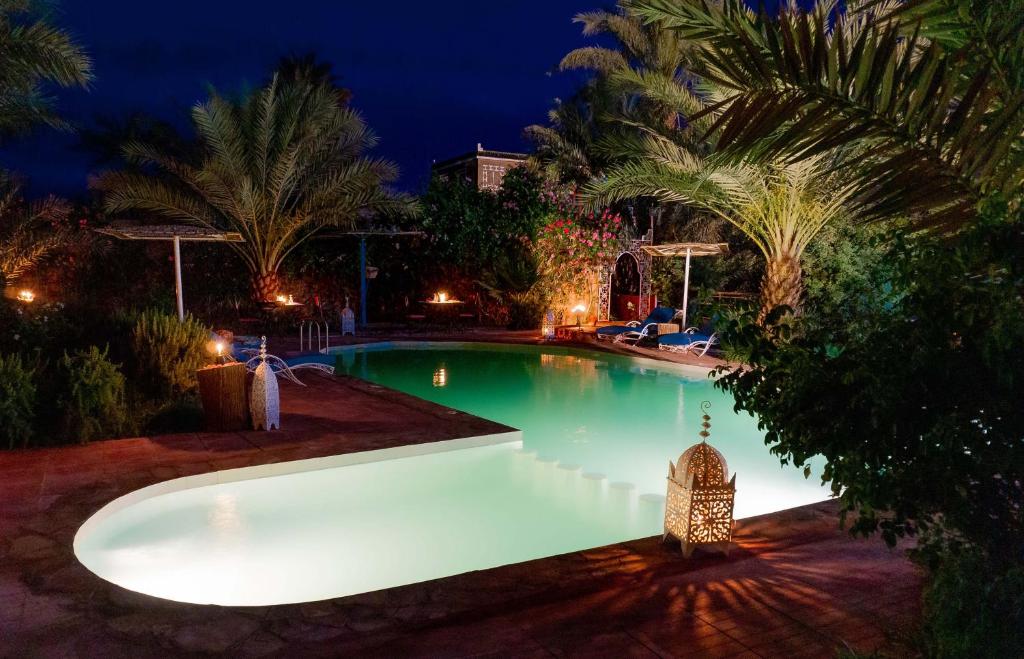 a swimming pool with lights in a backyard at night at Riad Zagora Palms in Zagora