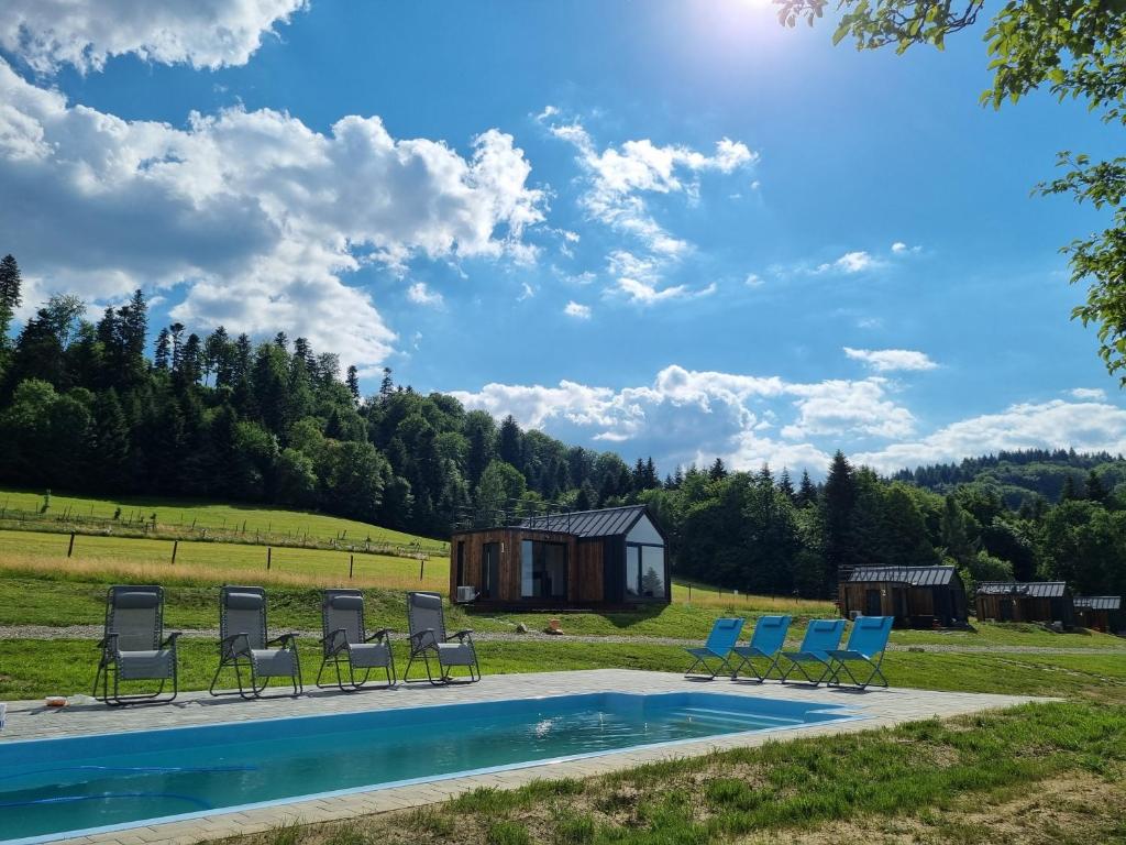 a pool with chairs and a house in the background at Klimkówka Pod Gwiazdami in Klimkówka