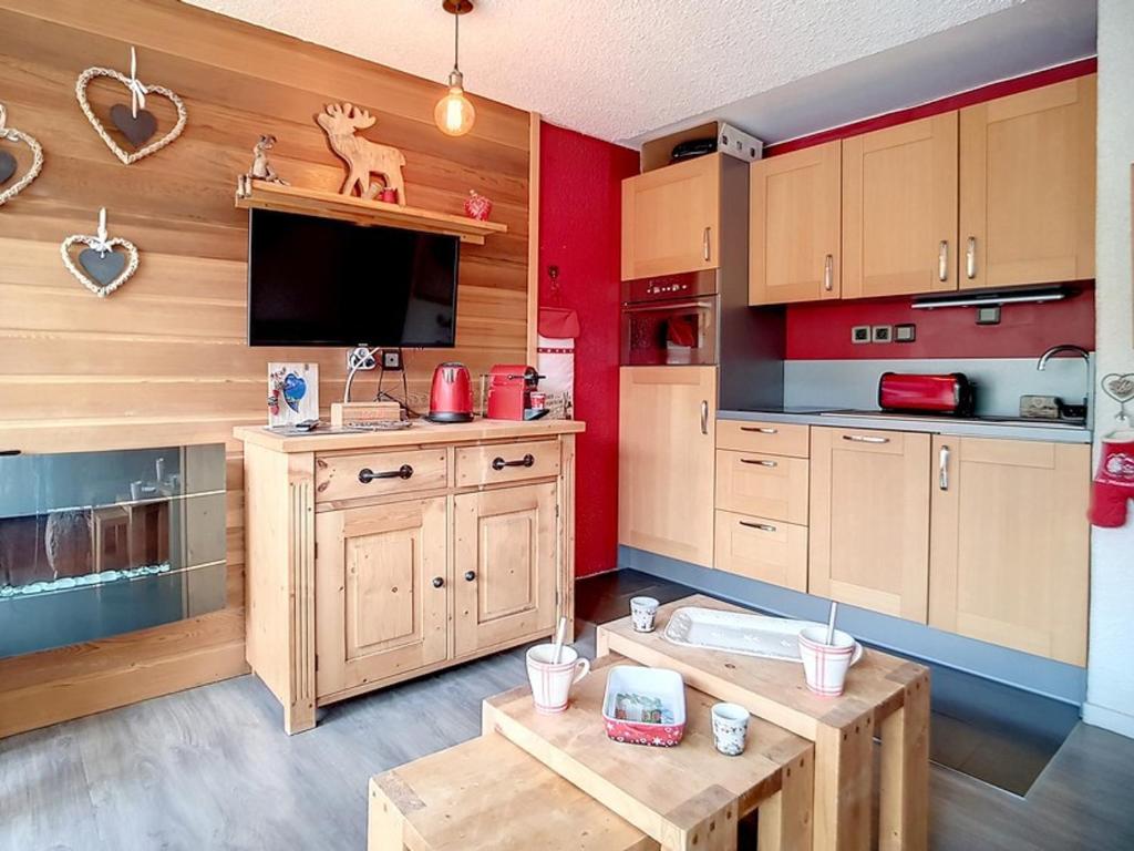 Il comprend une cuisine avec des placards en bois et une télévision murale. dans l'établissement Studio rénové aux Menuires, départ skis aux pieds - FR-1-344-840, aux Menuires