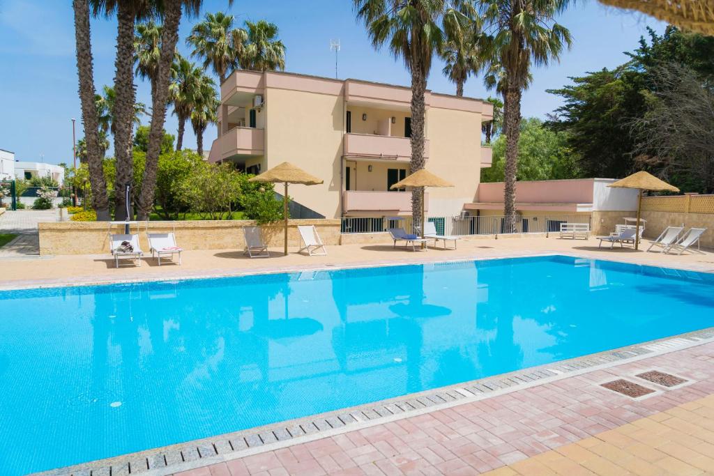 una piscina frente a un hotel con palmeras en Vaia Residence, en Torre dell'Orso