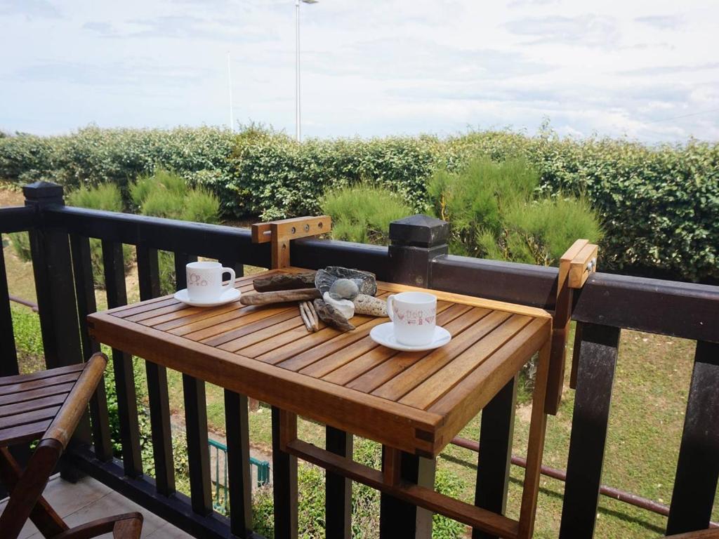 - une table en bois avec 2 tasses de café sur le balcon dans l'établissement Appartement Merville-Franceville-Plage, 2 pièces, 4 personnes - FR-1-465-62, à Merville-Franceville-Plage