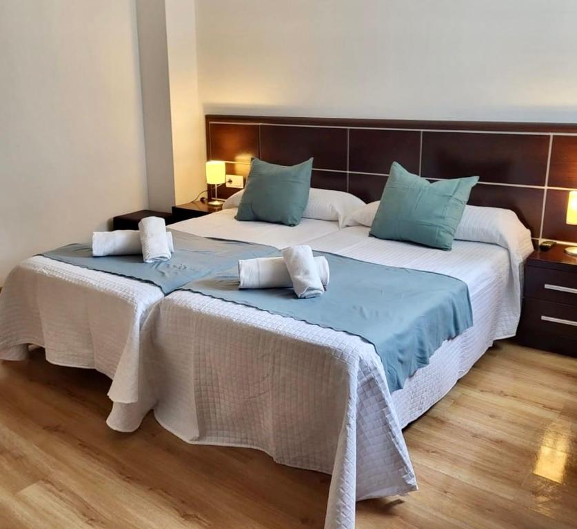 a bedroom with two beds with white sheets and blue pillows at Pension Orois in Melide