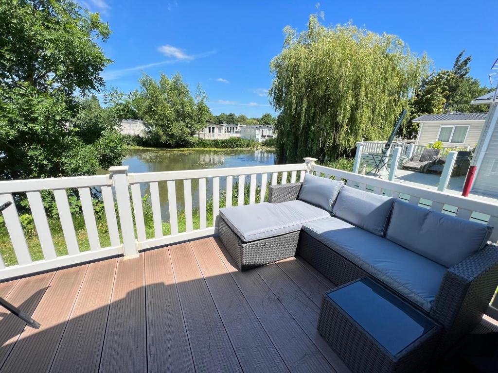 a couch on a deck with a view of a river at Dragonfly Lodge in South Cerney