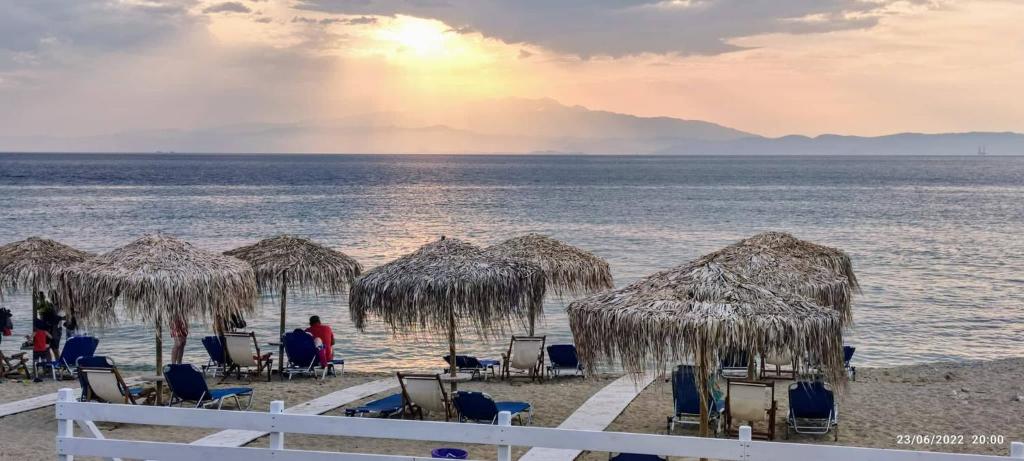 una spiaggia con sedie, ombrelloni di paglia e l'oceano di Villa Giotis Suite a Skala Sotiros