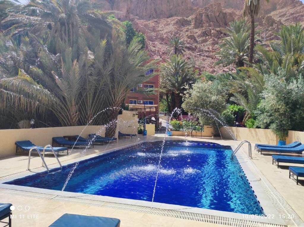 a pool with palm trees and a mountain in the background at Auberge Camping Atlas in Tinerhir