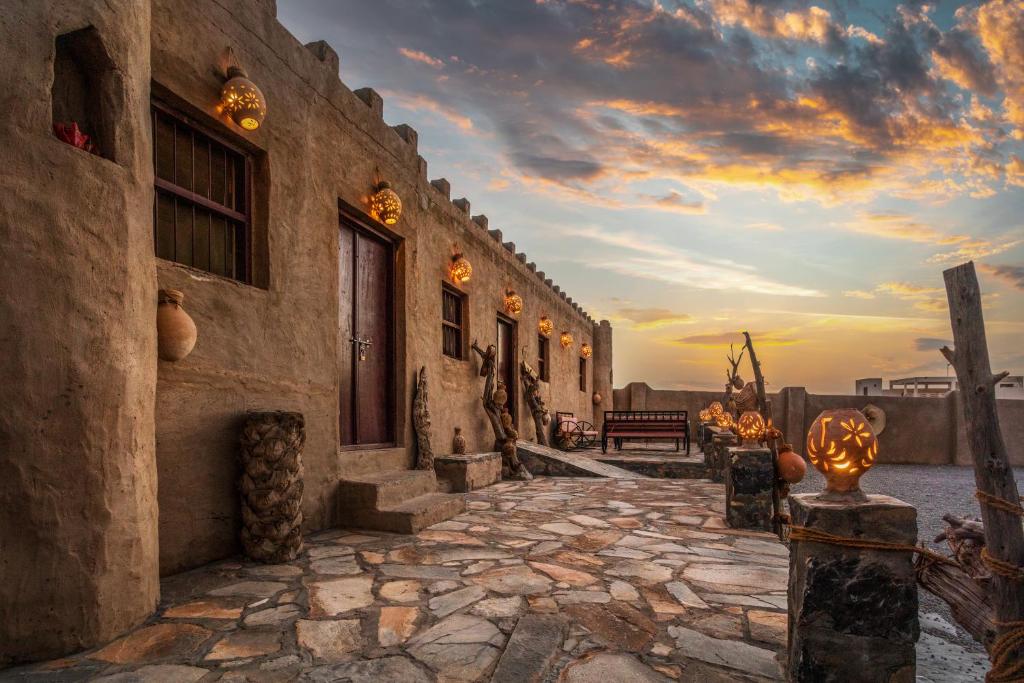 a building with a stone walkway with a sunset in the background at Canyon Rest House Jabal Shams in Al Ḩamrāʼ