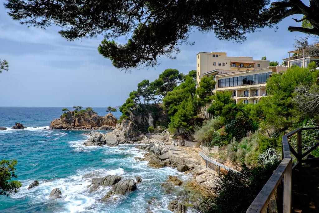 a building on a cliff next to the ocean at Hotel Cap Roig by Brava Hoteles in Platja d'Aro