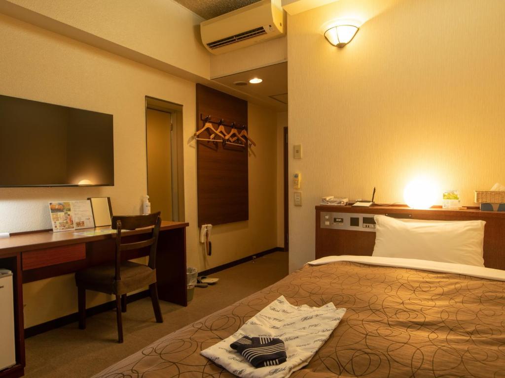 鹿児島市にあるホテルユニオンのベッド、デスク、テレビが備わるホテルルームです。