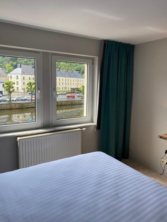 a bedroom with a bed and two windows at Hotel LA PLAGE in Bouillon