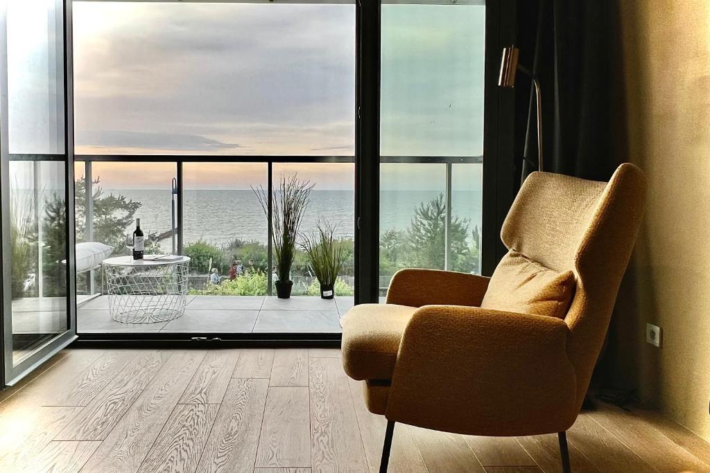 Sala de estar con silla y vistas al océano en Tuż przy plaży - nowoczesny apartament z tarasem i pięknym widokiem na Bałtyk, en Mielno