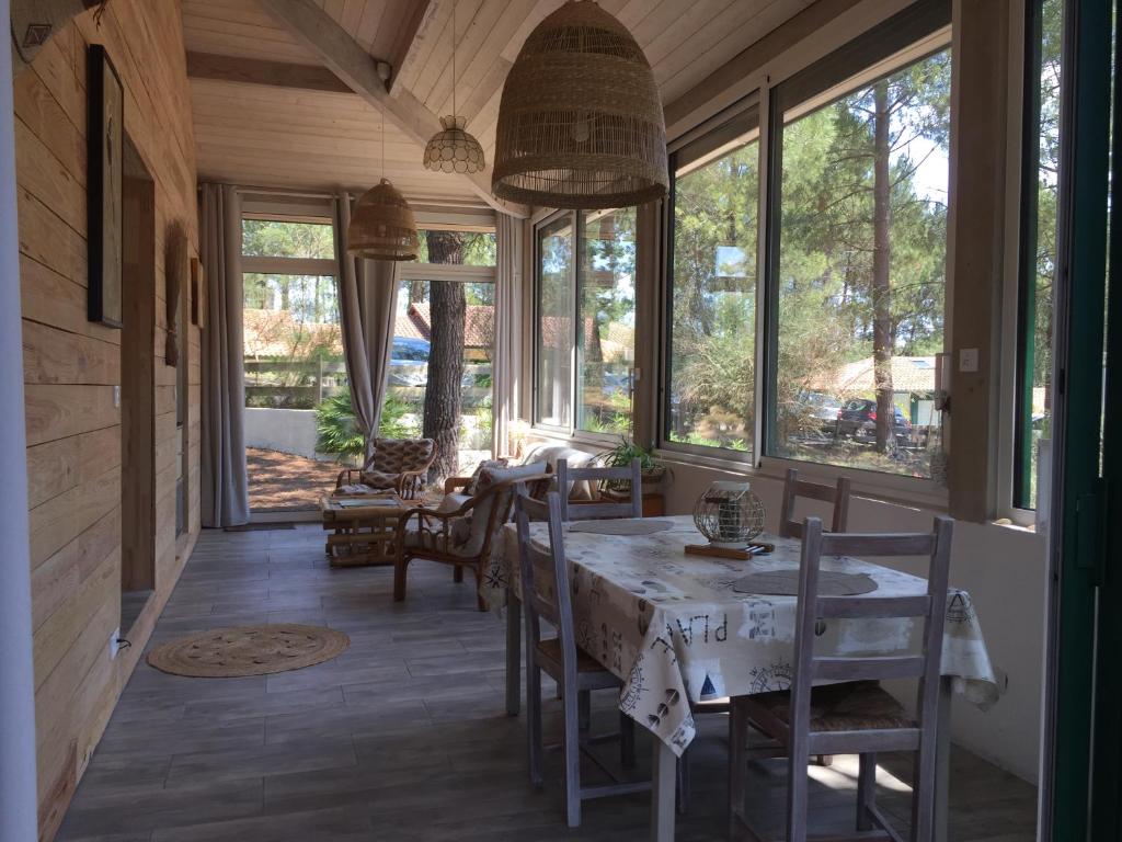 une salle à manger avec une table, des chaises et des fenêtres dans l'établissement Maison zen, à Moliets-et-Maa