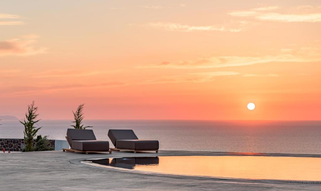 een zwembad met 2 ligstoelen en de oceaan bij zonsondergang bij Saint Apostles Villas in Fira