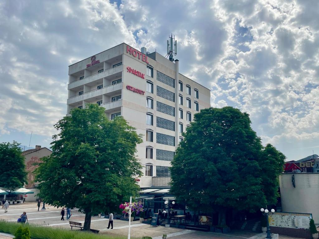 ein hohes weißes Gebäude mit Bäumen davor in der Unterkunft Spa Hotel Spartak in Sandanski