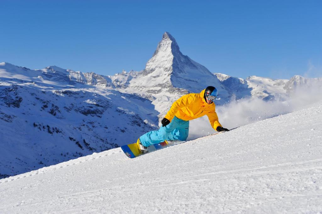 a man riding a snowboard down a snow covered slope at Alpenblick in Zermatt