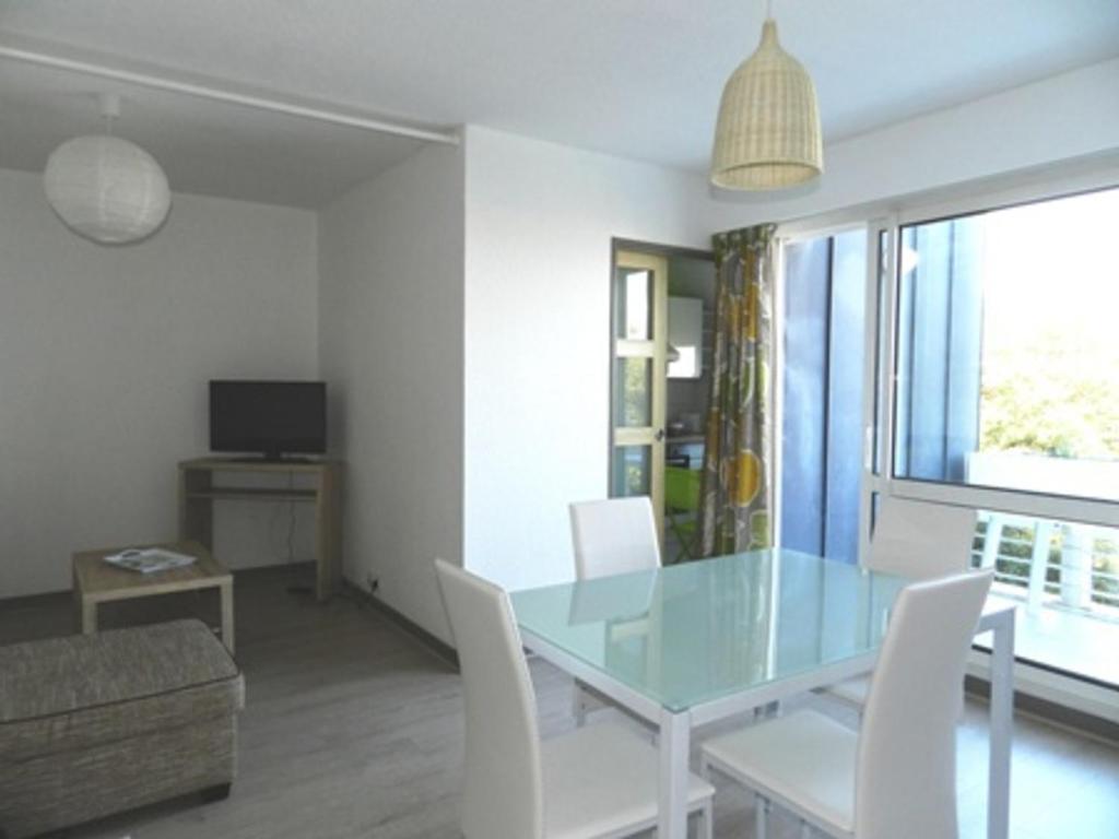 une salle à manger avec une table en verre et des chaises blanches dans l'établissement Appartement 2 Pièces à La Rochelle avec Balcon, Proche Plage des Minimes et Port, Parking Inclus - FR-1-551-7, à La Rochelle