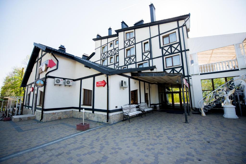 un edificio blanco y negro con dos bancos fuera en Trio Hotel Restaurant, en Ivano-Frankivsk