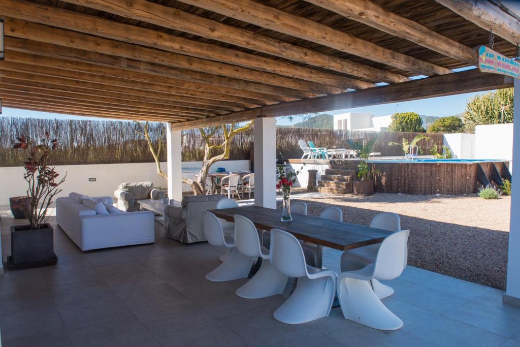 un patio con mesa de madera y sillas blancas en CASA ENTERA SA CALETA!!, en Sant Josep de sa Talaia