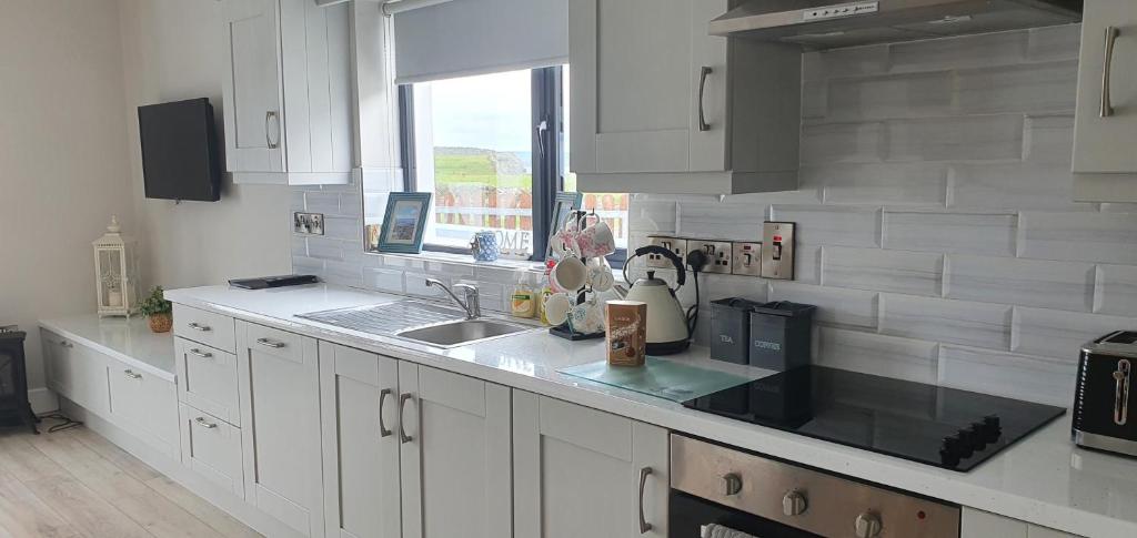a kitchen with white cabinets and a sink and a window at Beside the sea & minutes from Cliffs-Clahane Shore Lodge in Liscannor
