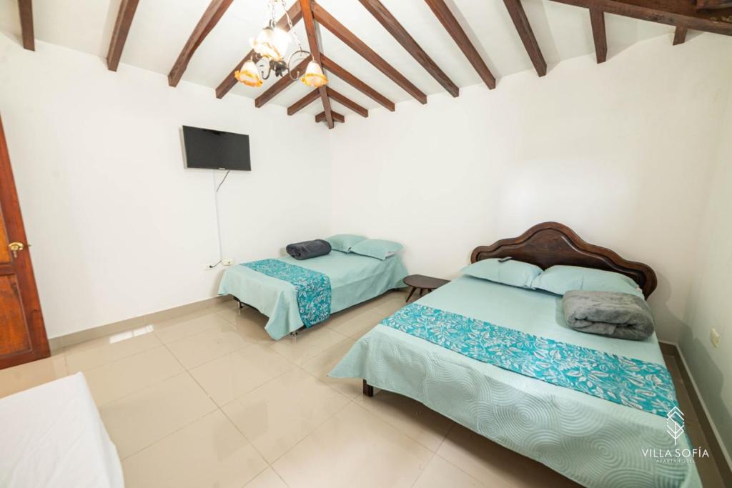 a bedroom with two beds and a tv on the wall at Aparta Hotel Villa Sofia in Jericó