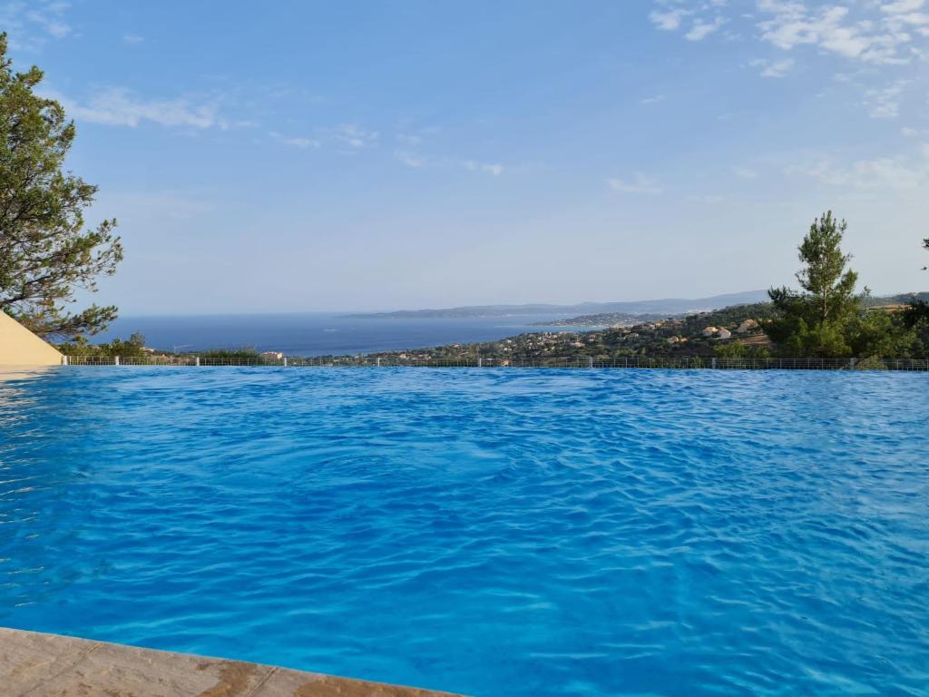 una grande piscina di acqua blu con alberi sullo sfondo di Appartement vue mer Golfe de Saint-Tropez a Les Issambres