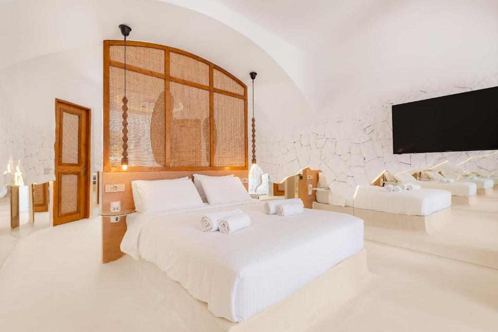 a white bedroom with a large bed and a flat screen tv at Faos Exclusive Suites in Ornos