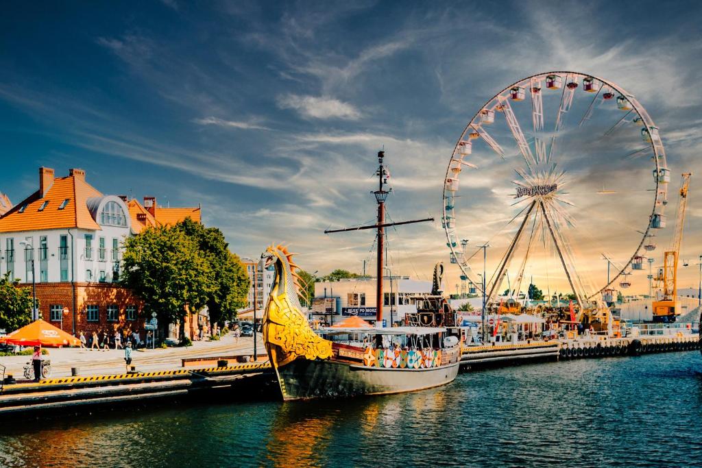 a ferris wheel and a boat in a body of water at Nadmorskie Tarasy Pink&Blue taras baseny siłownia sala zabaw in Kołobrzeg