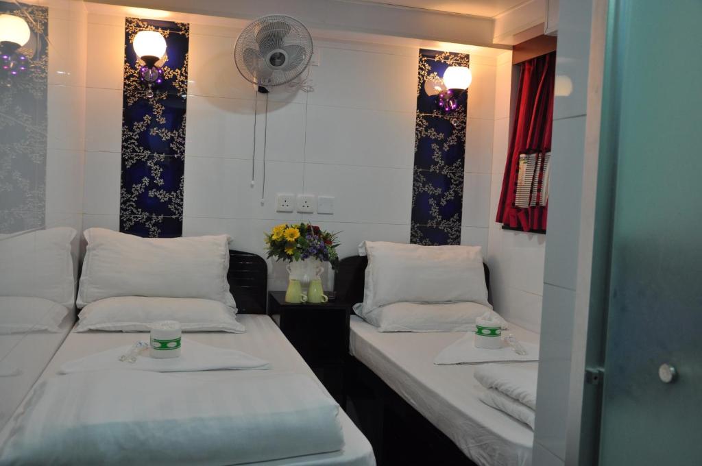 two beds in a room with flowers and a fan at New Guangzhou Guest House in Hong Kong