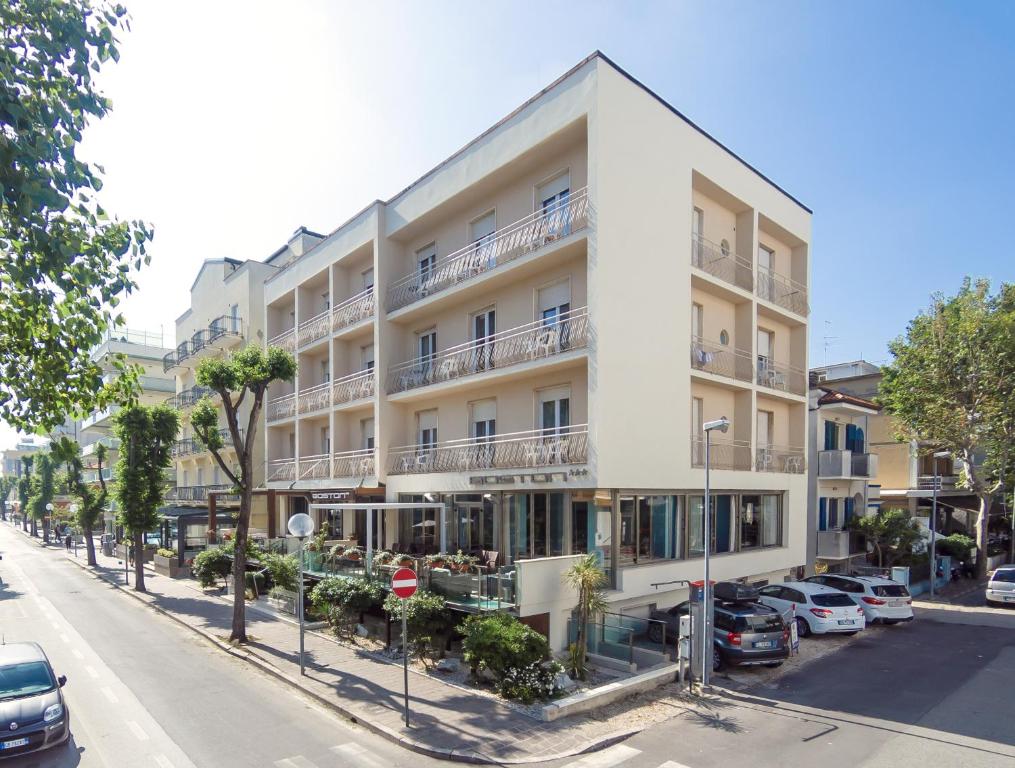 un edificio blanco en una calle con coches aparcados delante en Hotel Boston, en Cattolica