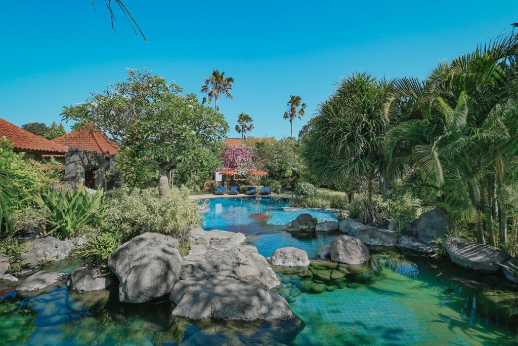 una piscina en un jardín con rocas y árboles en Parigata Villas Resort en Sanur