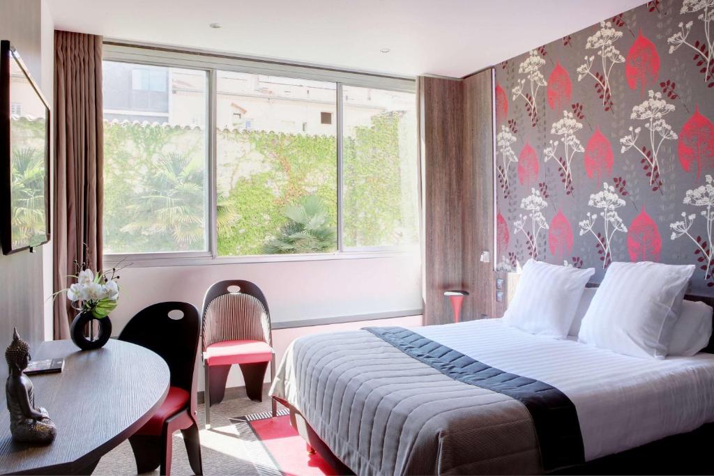 a hotel room with a bed and a table and a window at Best Western Premier Le Patio des Artistes Wellness Jacuzzi in Cannes