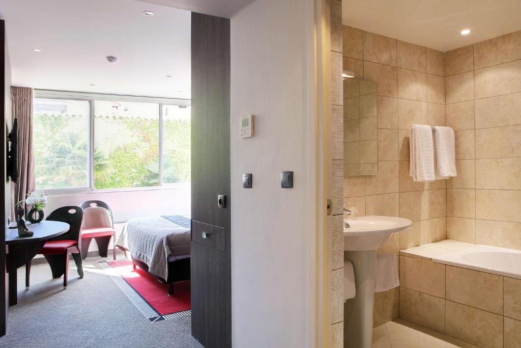 a bathroom with a sink and a tub and a bedroom at Best Western Premier Le Patio des Artistes Wellness Jacuzzi in Cannes