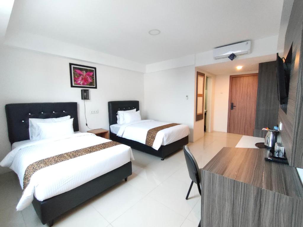 a hotel room with two beds and a desk at Golden Ganesha Hotel Yogyakarta by Ecommerceloka in Gondowulung