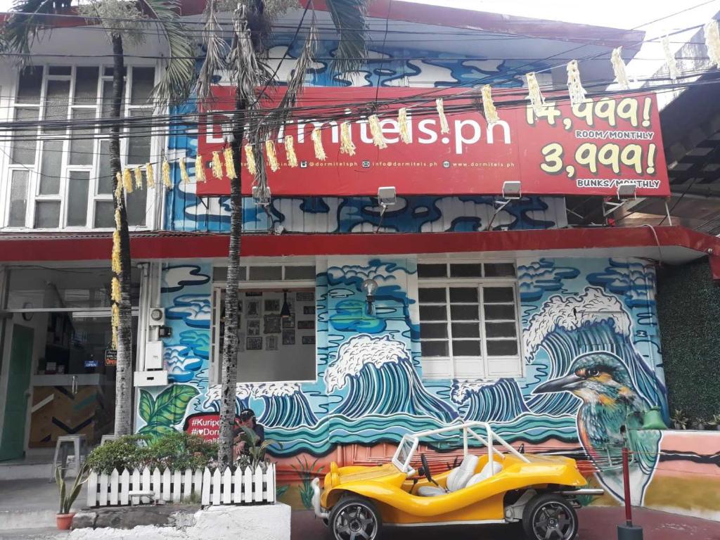 une voiture jaune garée devant un bâtiment avec une fresque murale dans l'établissement Dormitels.ph The Fort BGC, à Manille