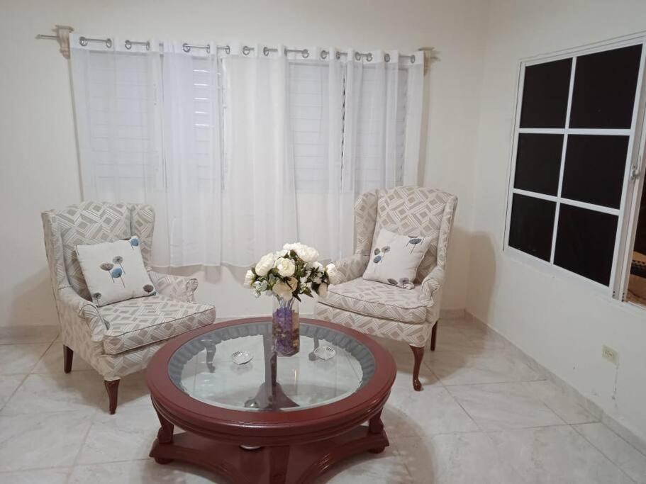 a living room with two chairs and a table with a vase of flowers at La Casa de Mamá in San Fernando de Monte Cristi