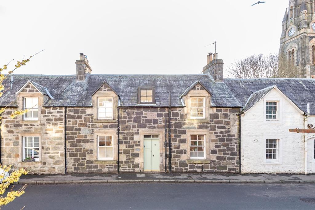 una antigua casa de piedra con una torre de reloj en el fondo en Charming Cardoon Cottage in beautiful village, en Comrie