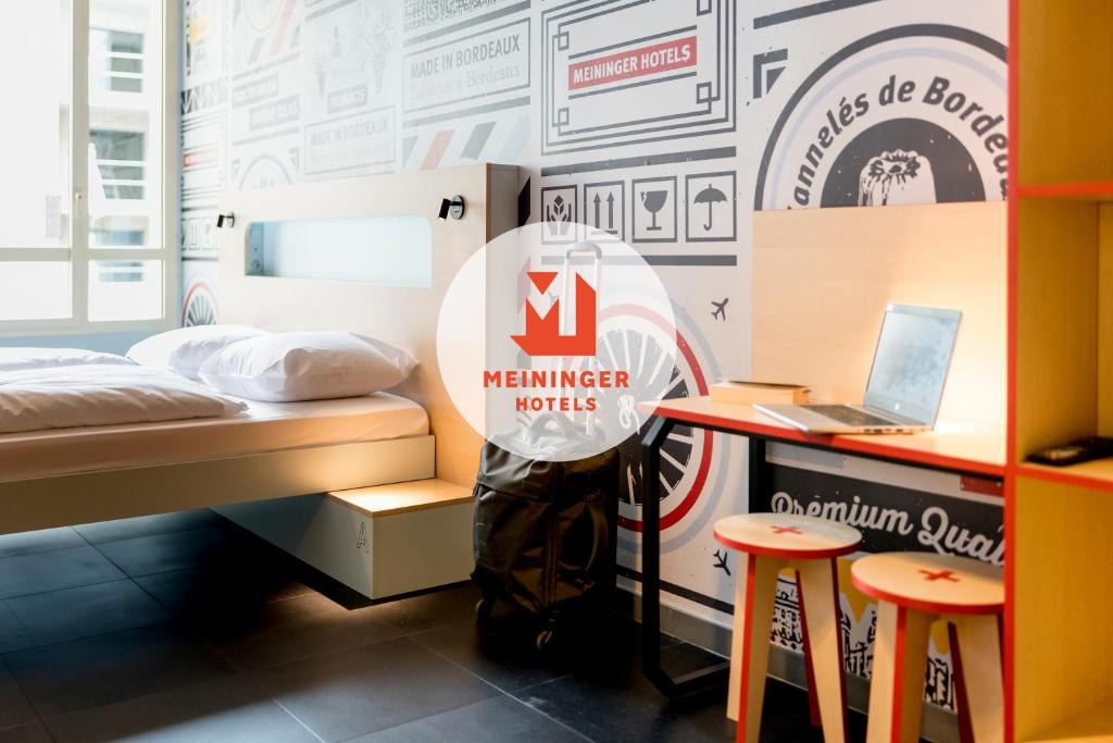 a room with a bed and a desk with a laptop at MEININGER Hotel Bordeaux Gare Saint-Jean in Bordeaux