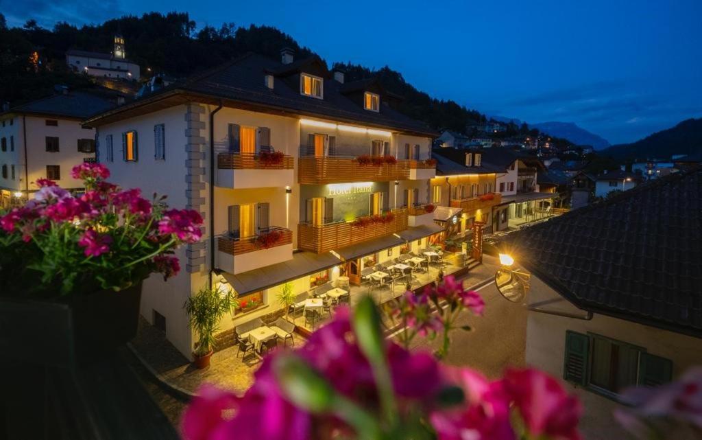 a view of a building at night with pink flowers at Hotel Italia in Castello di Fiemme