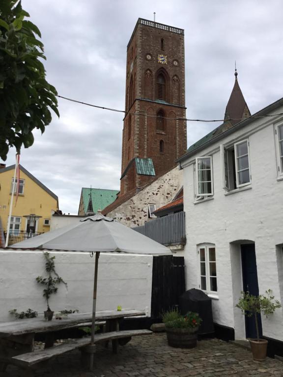 a table with an umbrella next to a building with a clock tower at Rebslagerhuset in Ribe