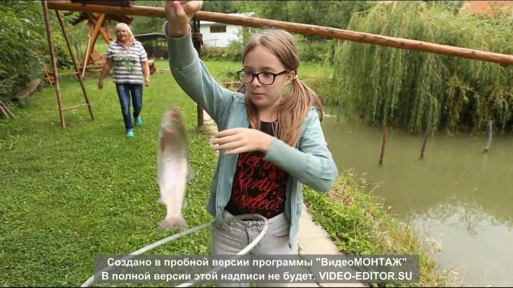 a girl holding a fish in front of a river at Котедж "Хата Рибака" in Kosiv
