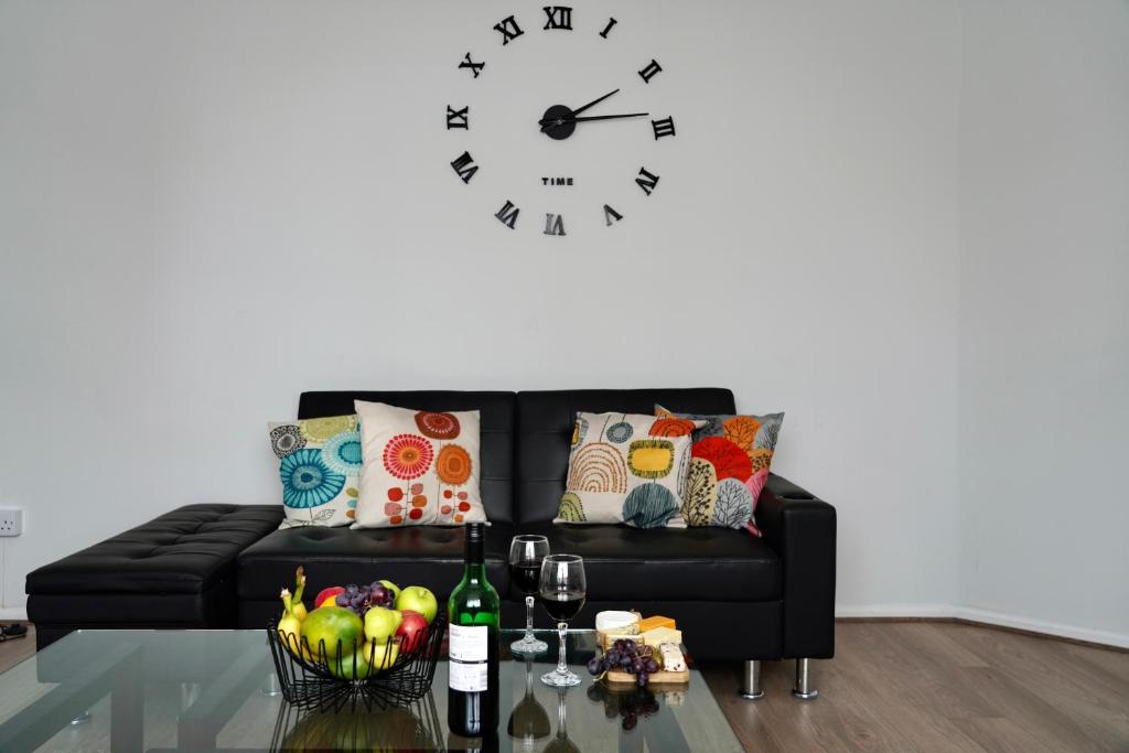 a living room with a black couch and a clock at JDB Chesterfield 3 Bedroom House in Whitton