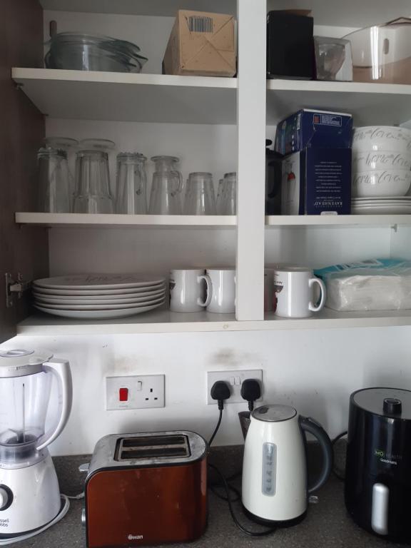 a kitchen counter with dishes and appliances on shelves at Our Guests Are Royal (KE) in Higham Ferrers