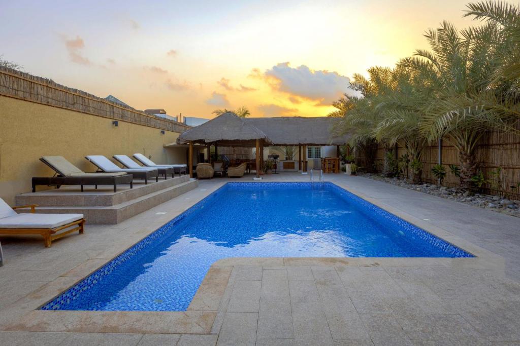 a large blue swimming pool with chairs and a house at Dar 66 Pool Villa with Jacuzzi in Ras al Khaimah