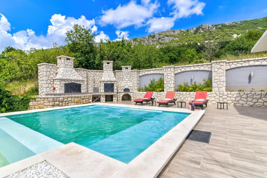 una piscina con sillas rojas y una pared de piedra en Villa Mate and Franka, en Bribir