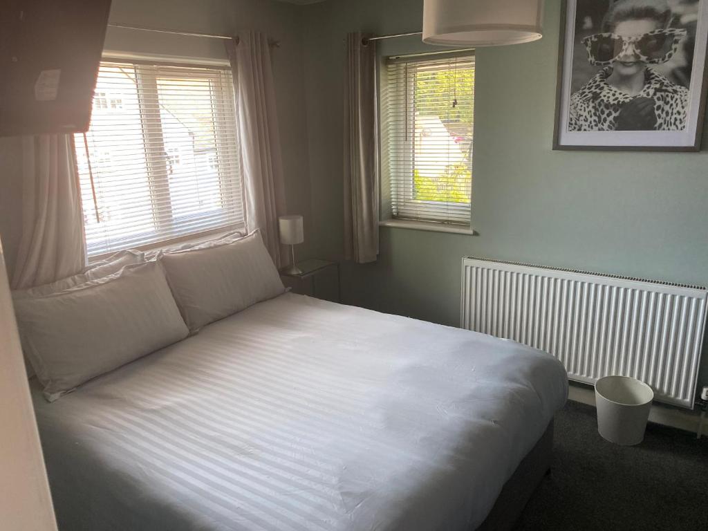 a bedroom with a white bed with two windows at Wellbrook Rooms in Tring