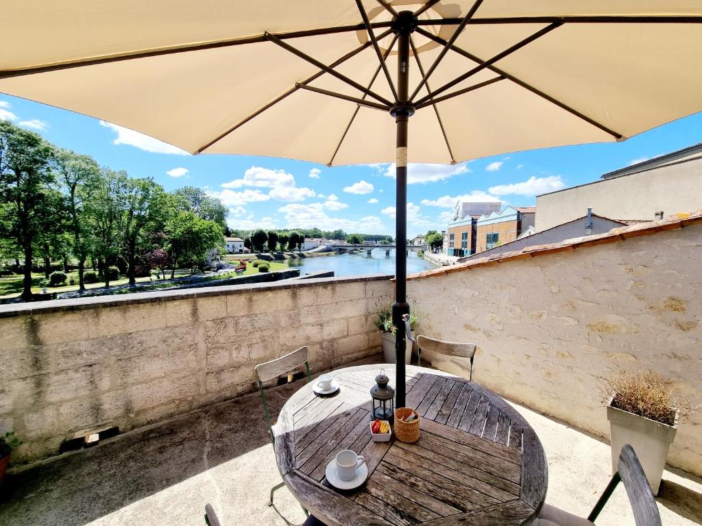 a wooden table with an umbrella and a river at QUAI 3 loft moderne et lumineux les pieds dans l'eau in Jarnac