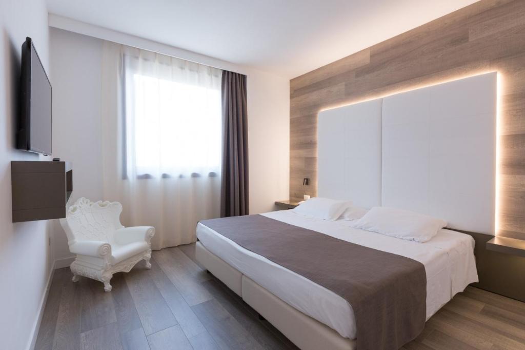 a bedroom with a large bed and a white chair at City Hotel & Suites in Foligno