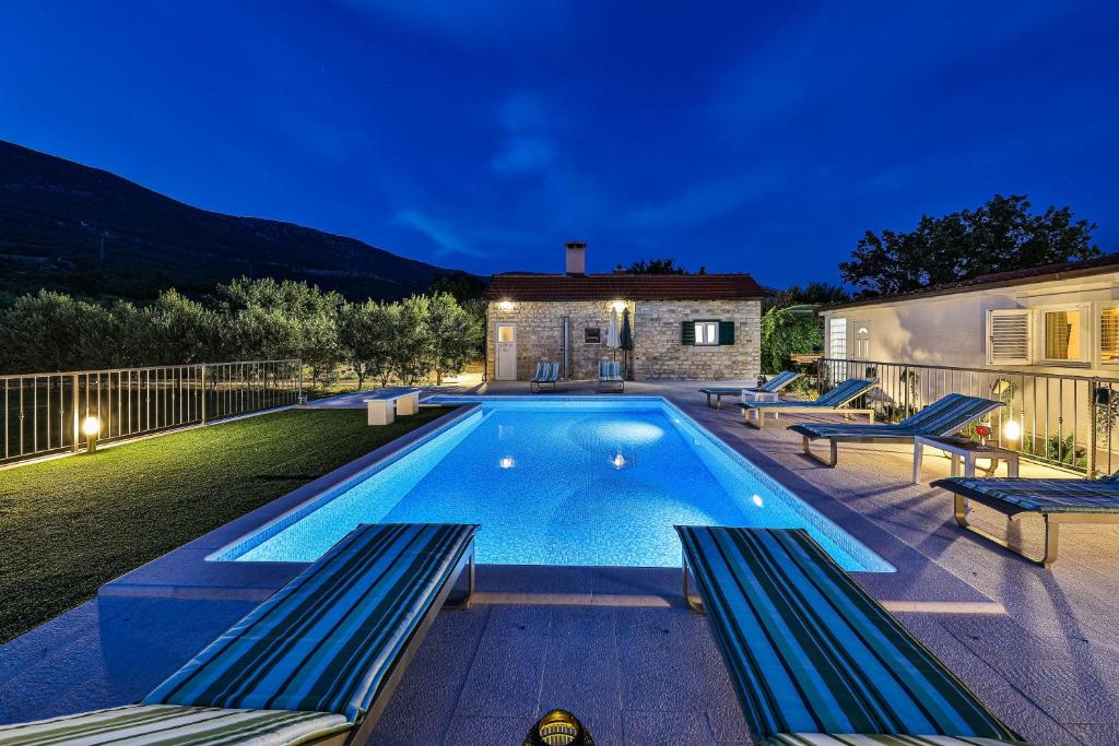 una piscina con 2 bancos junto a una casa en Home Away from home with outdoor pool, botanical garden and a beautiful sea view, en Kaštela